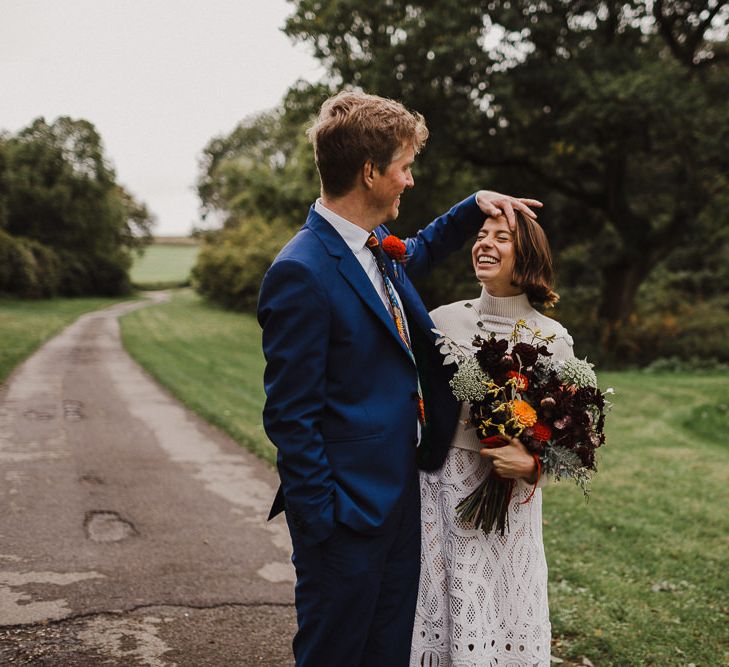 Groom in Navy Paul Smith Suit Combing His Bride in Crochet Wedding Dress Hair Out of Her Face