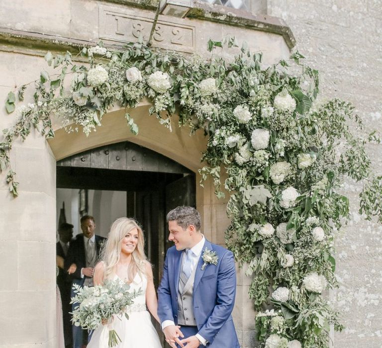 Bride in Sassi Holford wedding dress and groom in classic suit exiting the church