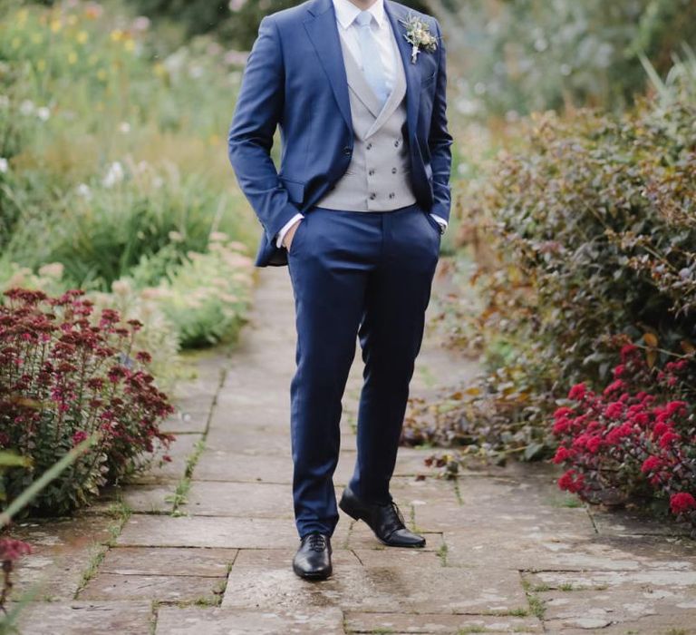 Groom in Navy suit with grey waistcoat standing in aAskham Hall  gardens