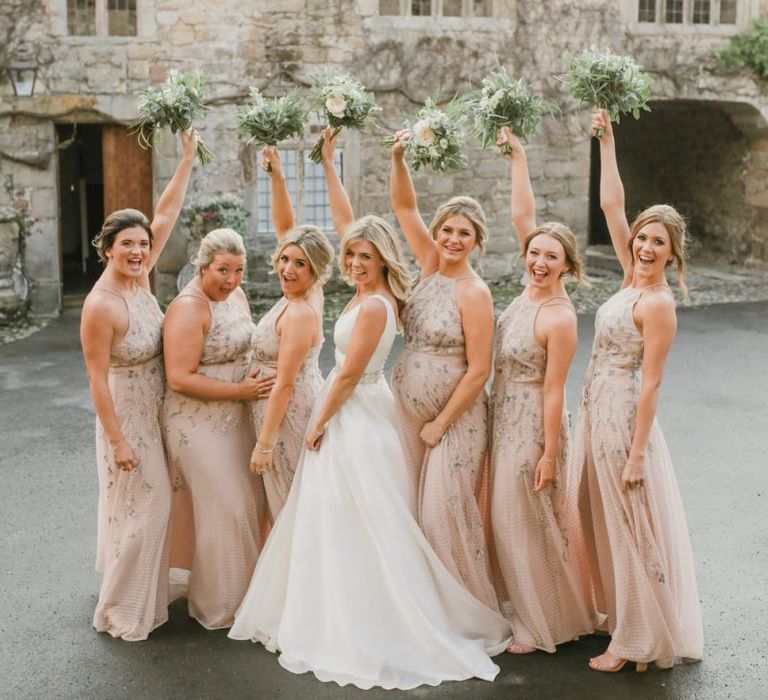 Bridal party portrait with bride and bridesmaids holding their bouquets in the air