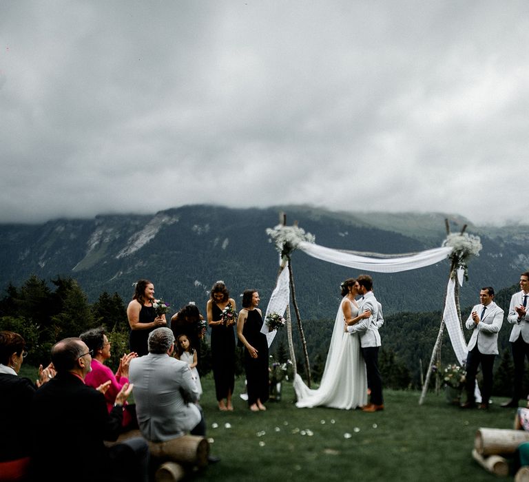 Bride in Mariées Passion Wedding Dress and Groom in Grey Blazer  Kissing at Their French Alp Wedding