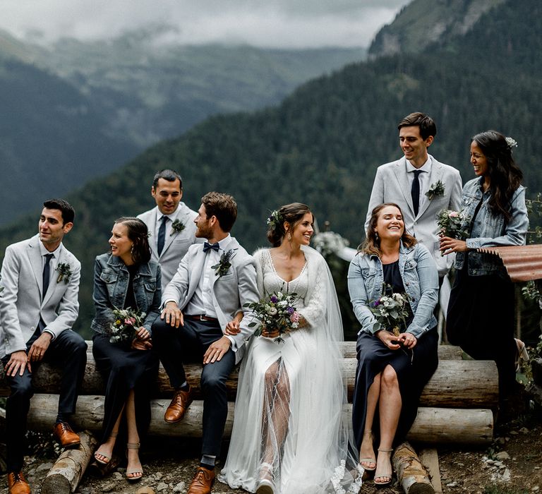 Wedding Party Picture in the French Alps with Bride in Mariées Passion Wedding Dress, Bridesmaids in Navy Dresses and Denim Jackets and Groomsmen in Grey Blazers and Navy Chinos