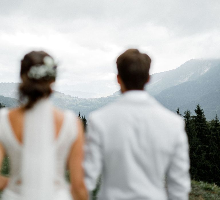 Bride in Mariées Passion Wedding Dress and Groom in Grey Blazer and Navy Chinos  Standing on the French Alps