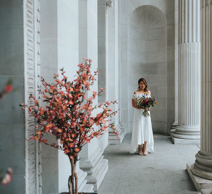 Bride in Lace Whistles Wedding Dress with High/Low Hem and Bardot Neckline | Bridal Bouquet with Bright Wild Flowers | Silver Sparkly Kurt Geiger Heels | High Street Wedding Dress for an Intimate Crouch End Pub Wedding with Bright Flowers | Miss Gen Photography