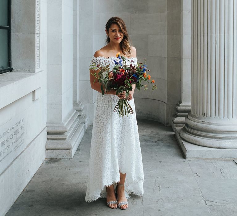 Bride in Lace Whistles Wedding Dress with High/Low Hem and Bardot Neckline | Bridal Bouquet with Bright Wild Flowers | Silver Sparkly Kurt Geiger Heels | High Street Wedding Dress for an Intimate Crouch End Pub Wedding with Bright Flowers | Miss Gen Photography