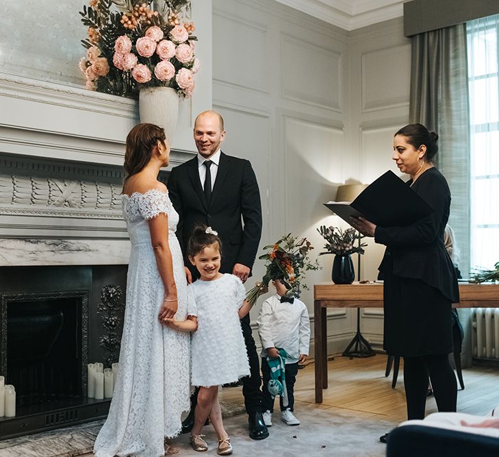 Bride in Lace Whistles Wedding Dress with High/Low Hem and Bardot Neckline | Groom in Black Reiss Jacket and Black Nudie Jeans with Church's Shoes | Flower Girl in White Zara Dress with Short Sleeves and Scoop Back | Page Boy in Zara Shirt, Trousers and Bow Tie | Wedding Ceremony at Old Marylebone Town Hall | High Street Wedding Dress for an Intimate Crouch End Pub Wedding with Bright Flowers | Miss Gen Photography