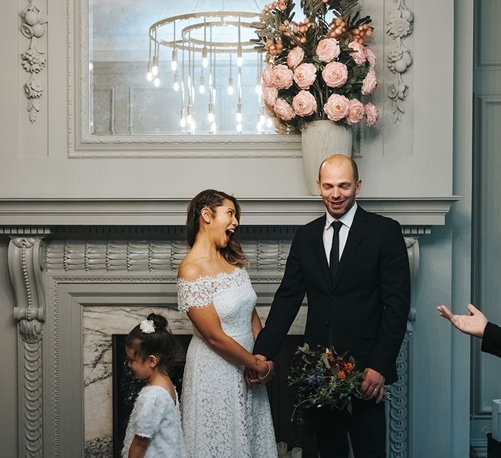 Bride in Lace Whistles Wedding Dress with High/Low Hem and Bardot Neckline | Groom in Black Reiss Jacket and Black Nudie Jeans with Church's Shoes | Flower Girl in White Zara Dress with Short Sleeves and Scoop Back | Wedding Ceremony at Old Marylebone Town Hall | High Street Wedding Dress for an Intimate Crouch End Pub Wedding with Bright Flowers | Miss Gen Photography