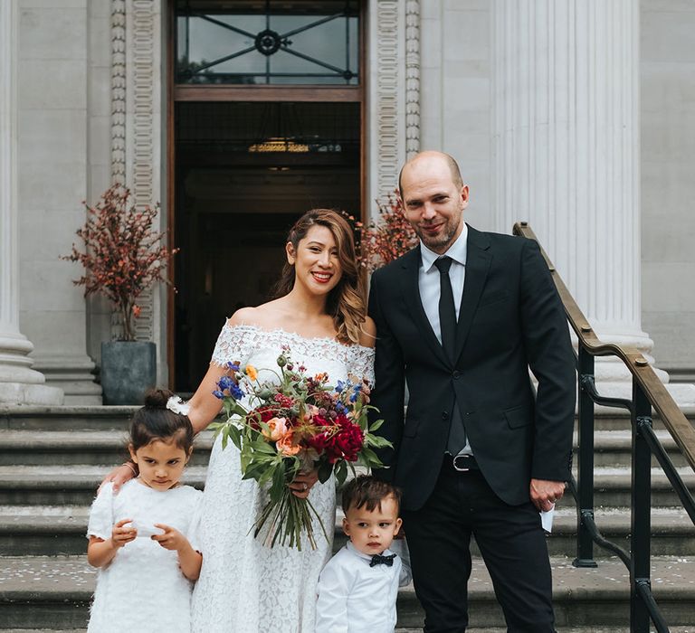 Bride in Lace Whistles Wedding Dress with High/Low Hem and Bardot Neckline | Groom in Black Reiss Jacket and Black Nudie Jeans with Church's Shoes | Flower Girl in White Zara Dress with Short Sleeves and Scoop Back | Page Boy in Zara Shirt, Trousers and Bow Tie | Bridal Bouquet with Bright Wild Flowers | Wedding Ceremony at Old Marylebone Town Hall | High Street Wedding Dress for an Intimate Crouch End Pub Wedding with Bright Flowers | Miss Gen Photography