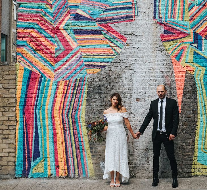 Bride in Lace Whistles Wedding Dress with High/Low Hem and Bardot Neckline | Silver Sparkly Kurt Geiger Heels | Groom in Black Reiss Jacket and Black Nudie Jeans with Church's Shoes | Bridal Bouquet with Bright Wild Flowers | High Street Wedding Dress for an Intimate Crouch End Pub Wedding with Bright Flowers | Miss Gen Photography