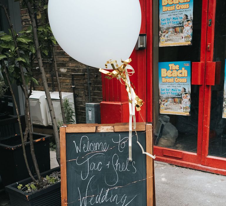 Chalkboard Welcome Sign | Oversized White Balloon with Gold Ribbon | Victoria Stakes Pub Wedding Reception | High Street Wedding Dress for an Intimate Crouch End Pub Wedding with Bright Flowers | Miss Gen Photography