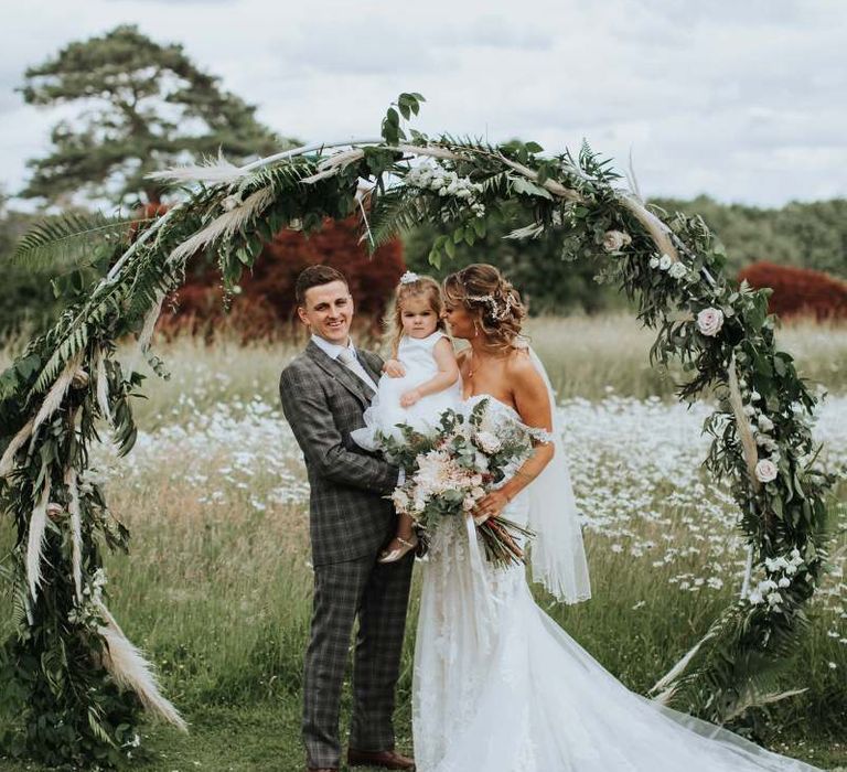 Bride and Groom With Daughter Under Moon Gate And Floral Backdrop