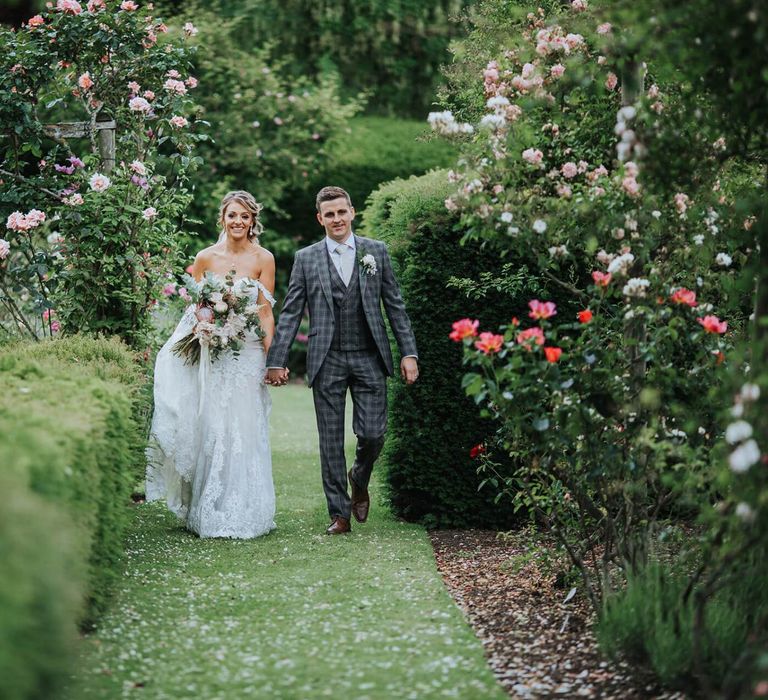 Bride and Groom Walk Through Grounds With Floral Backdrop