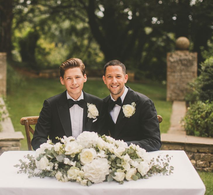 Groom and Groom Sitting at the Wedding Ceremony Table with White Floral Arrangement