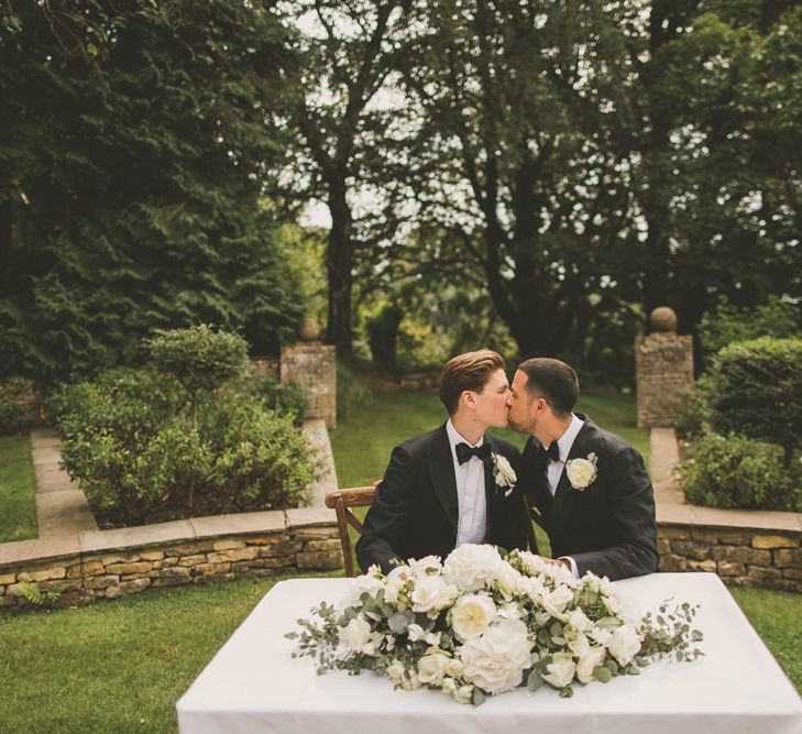 Groom and Groom Kissing at the Wedding Ceremony Table with White Floral Arrangement