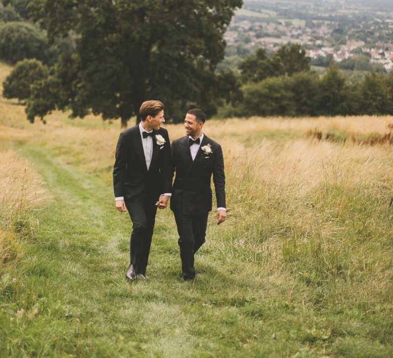 Two Grooms in Black Tie Suits Walking Through Fields