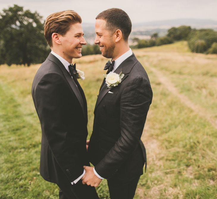 Portrait of Grooms in Tuxedos Smiling at Each Other Holding Hands in a Field