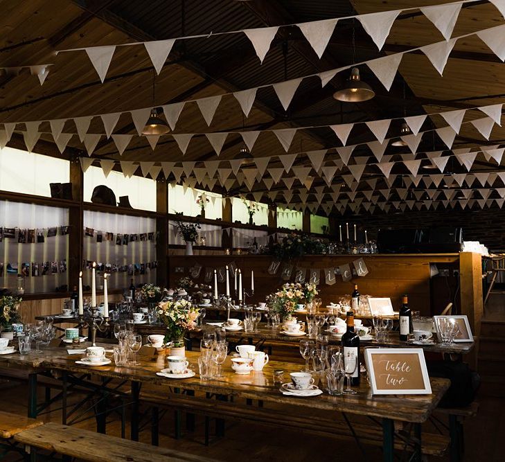 Wedding Reception Decor | On Site Pub at Fforest Farm | Long Wooden Tables and Benches | White Bunting | Flowers in Jam Jars | Tea Cups and Saucers | Candlesticks | Tapered Candles | Lace KatyaKatya Dress for Tipi Wedding at Fforest Farm | Claudia Rose Carter Photography