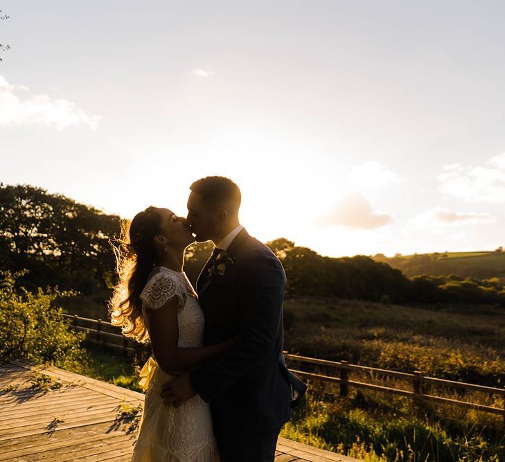 Bride in Laced KatyaKatya Wedding Dress with Cap Sleeves and Ribbon Belt | Groom in Blue T.M Lewin Suit with Navy Hawkes Bespoke Outfitters Waistcoat | Lace KatyaKatya Dress for Tipi Wedding at Fforest Farm | Claudia Rose Carter Photography