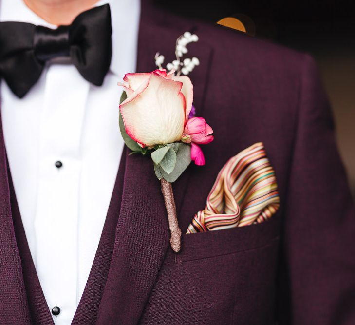 Groom wearing purple three piece suit with pink rose buttonhole