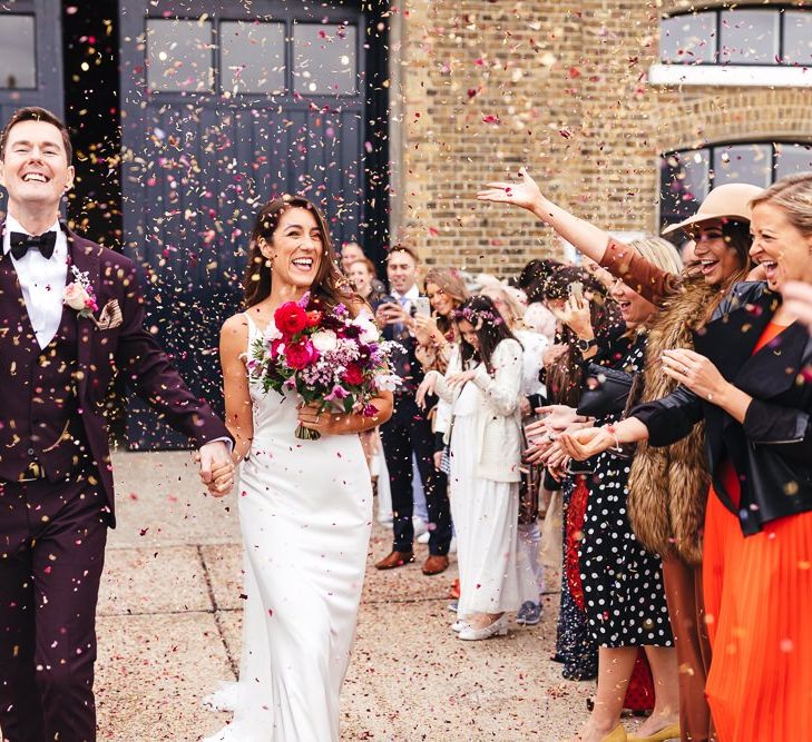 Bride clutching vibrant bouquet and groom wearing three piece suit