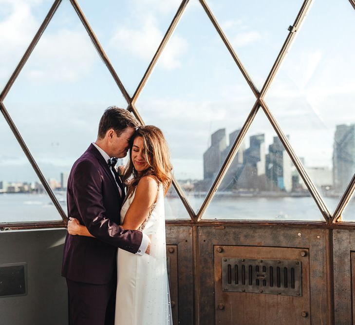 Bride and groom embrace at London celebration wearing three piece suit and beautiful dress with polka dot train