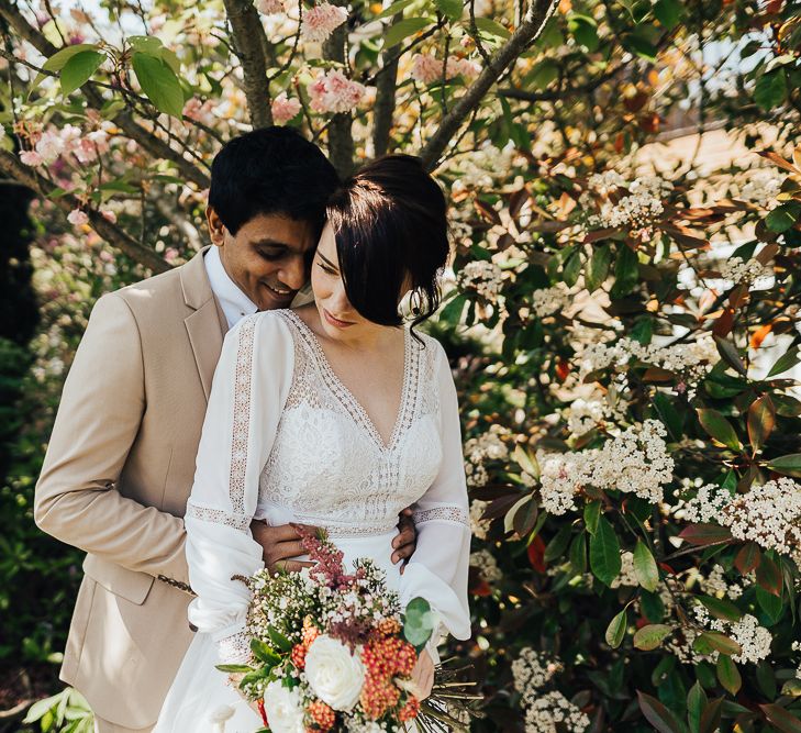 Groom embracing his bride in long sleeve wedding dress