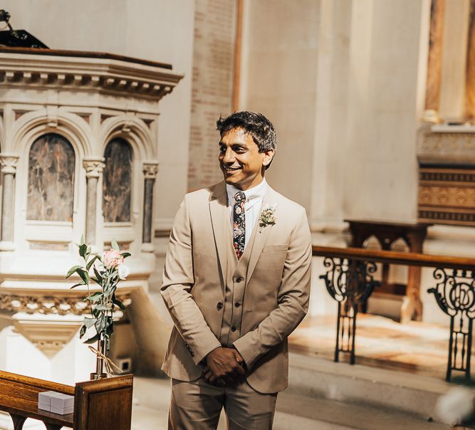 Groom in beige wedding suit with floral tie standing at the altar