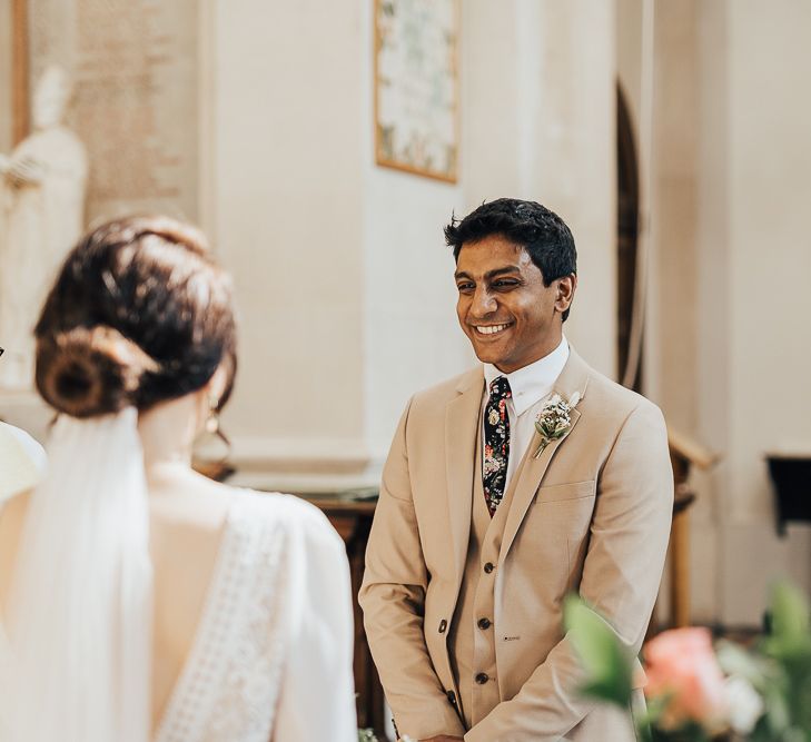 Groom in cream three-piece suit with floral tie smiling during wedding ceremony