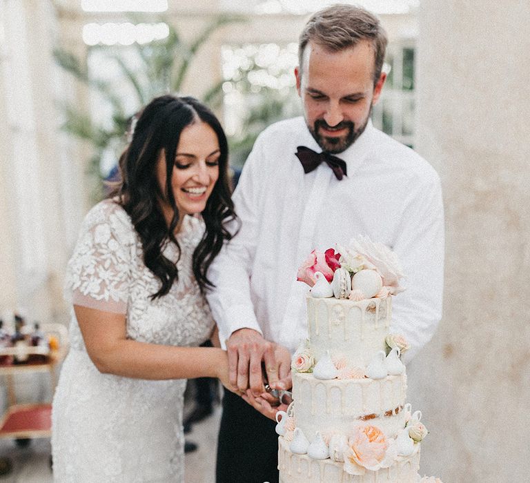 Cutting of Cake | Semi Naked Four Tier Drip Cake | Bride in Hermione de Paula Wedding Gown with Short Sleeves and Personalised Embroidery | Groom in Navy Lanvin Tuxedo and Black Burberry Shoes | Burgundy Bow Tie | Stunning Syon Park Wedding with Quill Stationery Suite | Nancy Ebert Photography