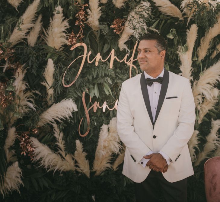 Groom in White Dinner Jacket Standing at the Greenery and Pampas Grass Altar