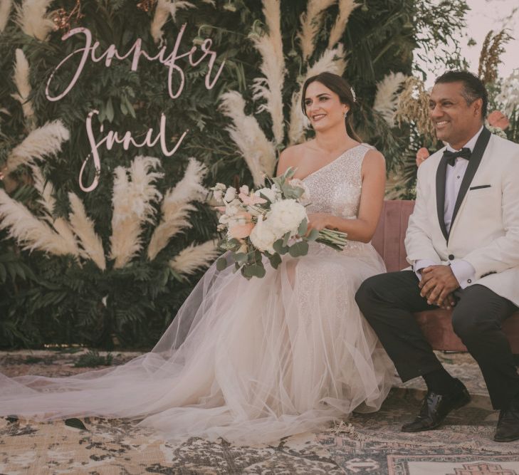 Bride and Groom Sitting at the Altar with Blush Velvet Love Seat, Wool Rug and Greenery and Pampas Grass Backdrop