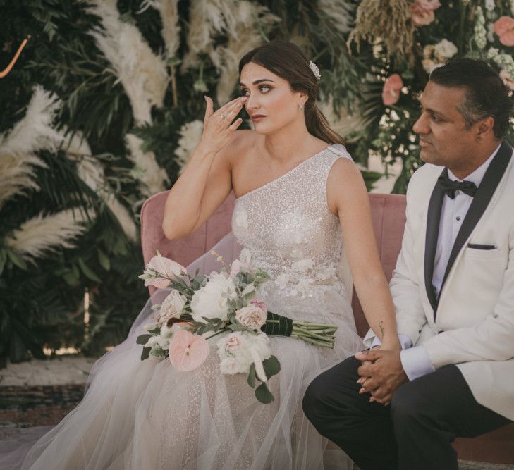 Emotional Bride in Once Shoulder Wedding Dress and Groom in White Dinner Jacket at the Wedding Ceremony