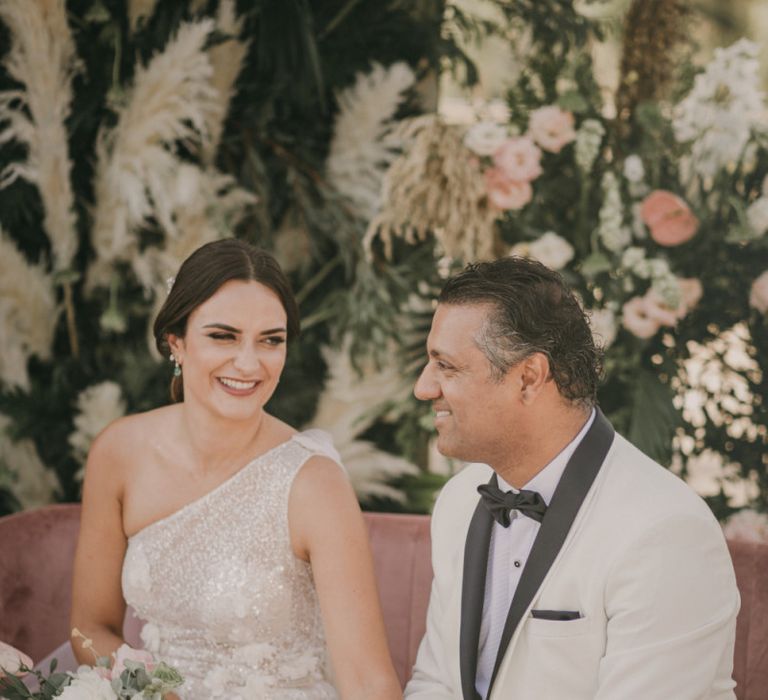 Bride in One Shoulder Wedding Dress and Groom in White Dinner Jacket Laughing During the Wedding Ceremony