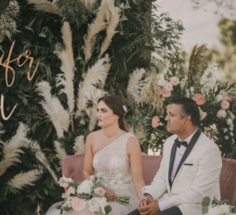 Bride in One Shoulder Wedding Dress and Groom in White Dinner Jacket Holding Hands During the Wedding Ceremony