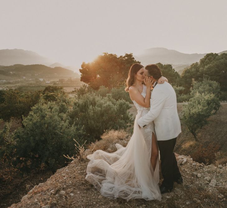 Bride in One Shoulder Muse by Berta Wedding Dress and Groom in White Dinner Jacket Standing on a Spanish Mountain