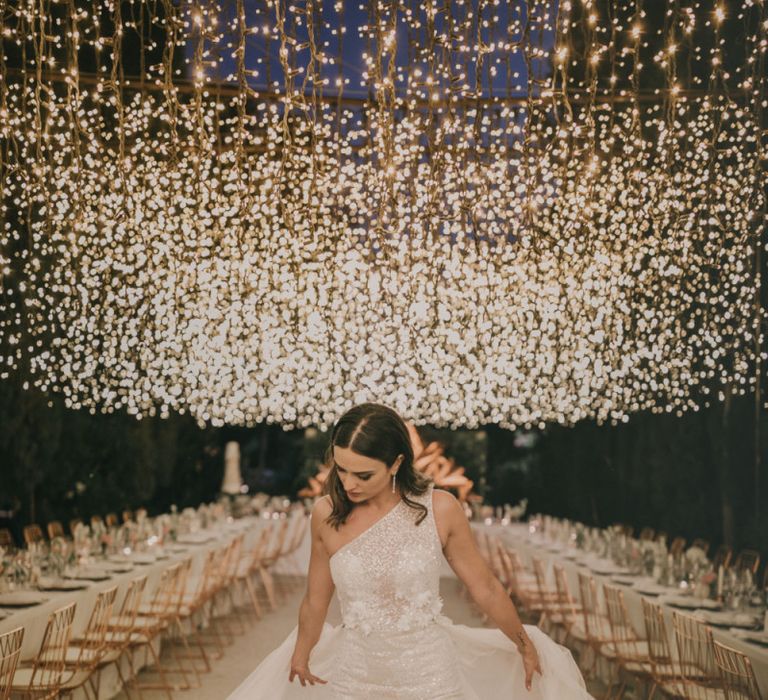 Bride in One Shoulder Muse by Berta Wedding Dress with Front Split Under a Fairy Light Canopy