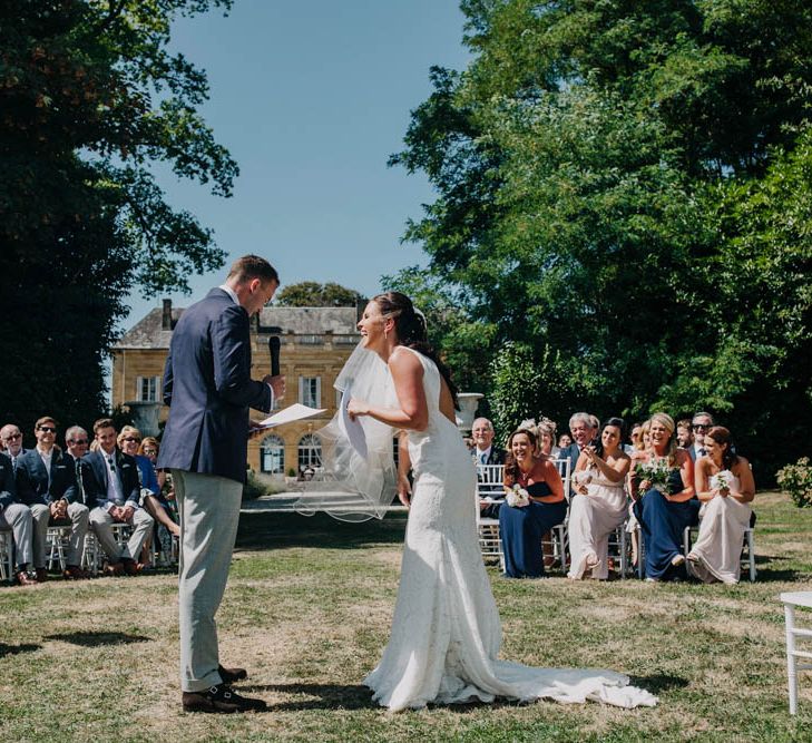 Bride in Lace Boat Neck Pronovias Wedding Dress with Keyhole Back and Fishtail Train | Fingertip Length Veil | Groom in Navy Jacket, Grey Trousers and White Shirt with Pink Tie from Suit Supply | Bridesmaids in Strapless Navy or Pink Dresses from ASOS | Outdoor Wedding Ceremony at Chateau La Durantie, Dordogne | Outdoor Seating Area and Macaroon Tower at French Chateau Wedding | Lush Imaging