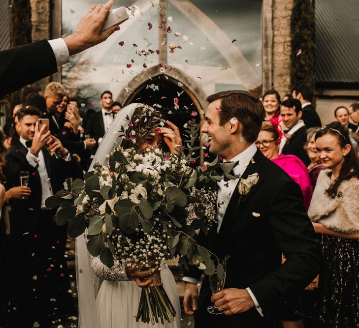 Confetti Moment with Bride in Made With Love Bridal Wedding Dress Holding a White and Green Bouquet and Groom in Tuxedo