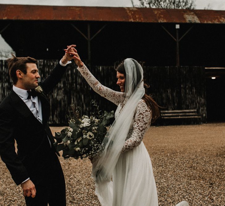 Groom in Tuxedo and Bow Tie Twirling his Bride in Made With Love Bridal Wedding Dress Holding a White and Green Bouquet