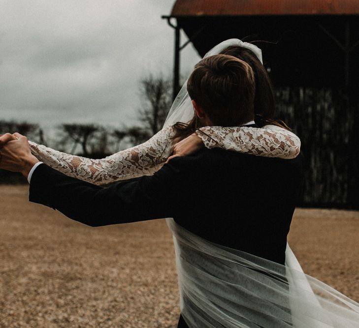 Groom in Tuxedo Twirling his Bride in Made With Love Bridal Wedding Dress with Lace Long Sleeves