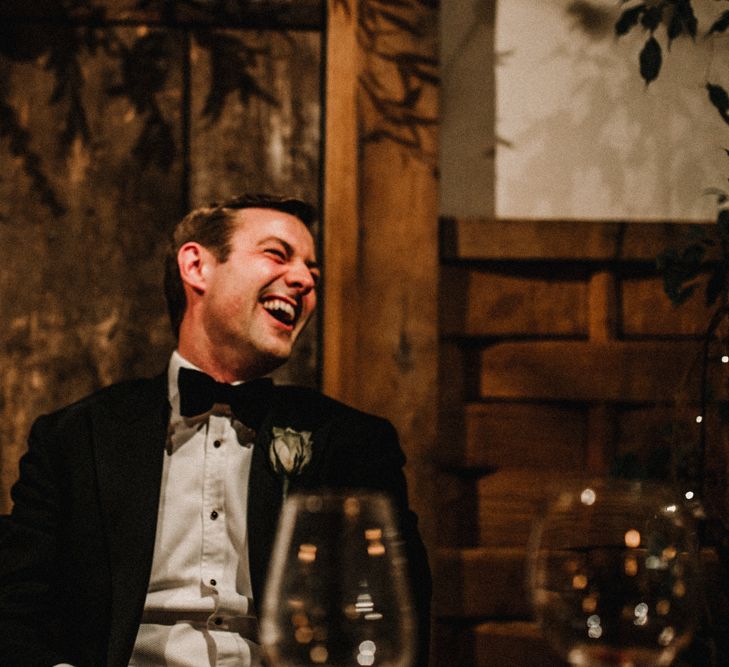 Groom in Tuxedo Laughing During Wedding Reception Speeches