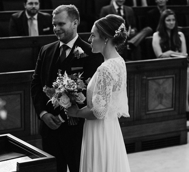 Bride in Charlie Brear Carenne Dress with Spaghetti Straps and Flowing Skirt | Bridal Lace Jacket by Charlie Brear | Bouquet of White and Blush Flowers with Foliage | Groom in Navy Three-Piece Suit with Blush Pocket Square | Town Hall Hotel Wedding Ceremony | Statement Floral Arrangement Altar and Potted Plants with Copper Frame Table Plan and Lace Jacket | Miss Gen Photography