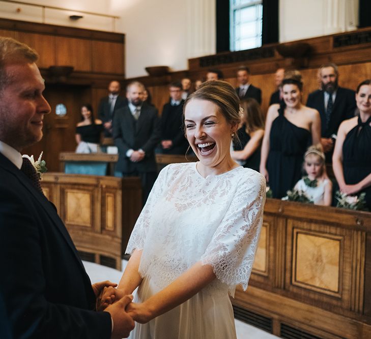 Bride in Charlie Brear Carenne Dress with Spaghetti Straps and Flowing Skirt | Bridal Lace Jacket by Charlie Brear | Groom in Navy Three-Piece Suit with Blush Pocket Square | Town Hall Hotel Wedding Ceremony | Statement Floral Arrangement Altar and Potted Plants with Copper Frame Table Plan and Lace Jacket | Miss Gen Photography