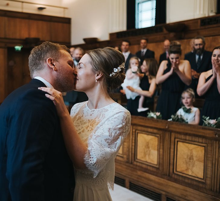 Bride in Charlie Brear Carenne Dress with Spaghetti Straps and Flowing Skirt | Bridal Lace Jacket by Charlie Brear | Porcelain Floral Hairpiece by Eden B |Groom in Navy Three-Piece Suit with Blush Pocket Square | Town Hall Hotel Wedding Ceremony | Statement Floral Arrangement Altar and Potted Plants with Copper Frame Table Plan and Lace Jacket | Miss Gen Photography