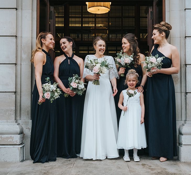 Bride in Charlie Brear Carenne Dress with Spaghetti Straps and Flowing Skirt | Bridal Lace Jacket by Charlie Brear | Bridesmaids in Navy Multiway Dresses from Debenhams | Flower Girl in White Dress | Wedding Bouquets of White and Blush Flowers with Foliage | Town Hall Hotel Wedding | Statement Floral Arrangement Altar and Potted Plants with Copper Frame Table Plan and Lace Jacket | Miss Gen Photography