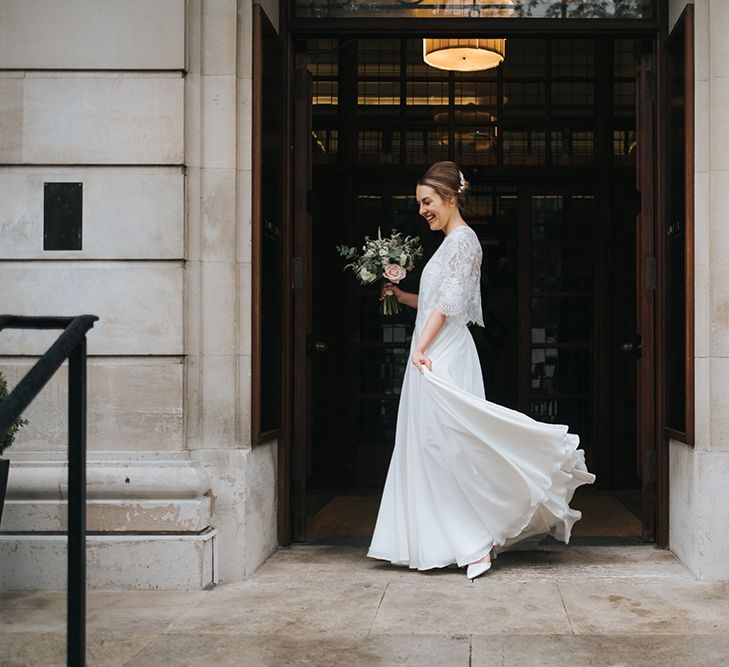 Bride in Charlie Brear Carenne Dress with Spaghetti Straps and Flowing Skirt | Bridal Lace Jacket by Charlie Brear | Porcelain Floral Hairpiece by Eden B | White Court Shoes from ASOS | Bouquet of White and Blush Flowers with Foliage | Town Hall Hotel Wedding | Statement Floral Arrangement Altar and Potted Plants with Copper Frame Table Plan and Lace Jacket | Miss Gen Photography