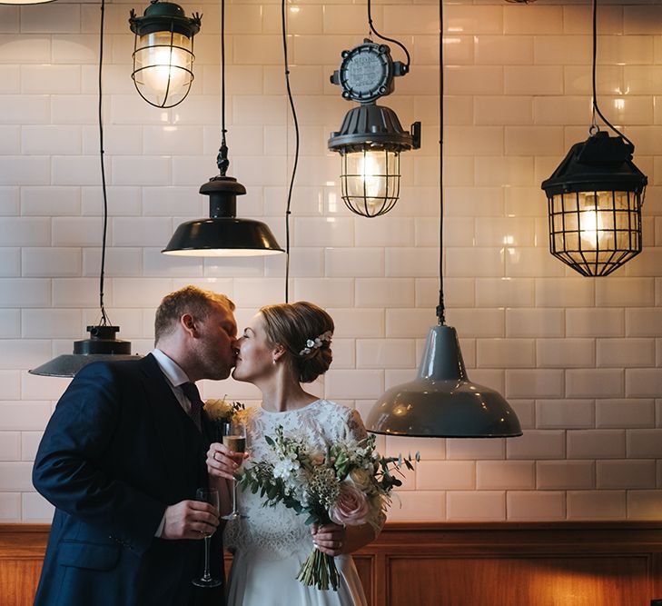 Bride in Charlie Brear Carenne Dress with Spaghetti Straps and Flowing Skirt | Bridal Lace Jacket by Charlie Brear | Porcelain Floral Hairpiece by Eden B | Bouquet of White and Blush Flowers with Foliage | Groom in Navy Three-Piece Suit with Blush Pocket Square | Hanging Lamps | Wedding Reception at Town Hall Hotel | Statement Floral Arrangement Altar and Potted Plants with Copper Frame Table Plan and Lace Jacket | Miss Gen Photography