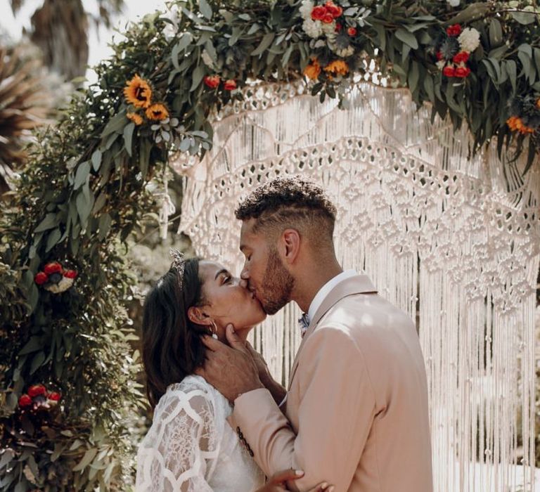 Groom on pale pink blazer kissing his bride in a Grace Loves Lace wedding dress