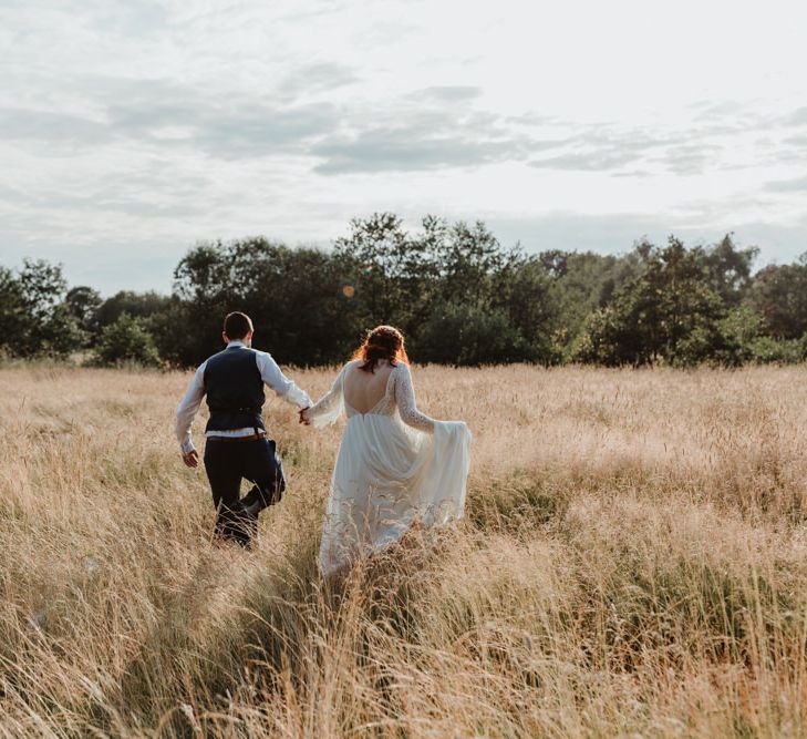 Bride and Groom Walk Through Meadow Holding Hands