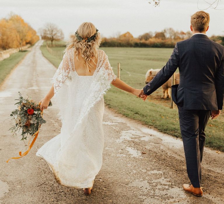 Groom in Navy Suit and Boho Bride in Grace Loves Lave Wedding Dress Holding Hands